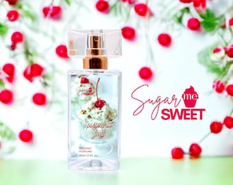 May include: A clear rectangular perfume bottle with a gold-coloured cap and a spray nozzle. The bottle features an image of pistachio fluff with a cherry on top. The text "Sugar me Sweet" and "pistachio fluff" are visible. The background has red berries.
