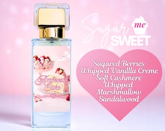 May include: A clear perfume bottle with a gold cap and a label featuring a pink cake design. The label reads "Ambrosia Cake" and lists scent notes like sugared berries and whipped vanilla creme. The background is pink.