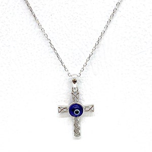 May include: Sterling silver necklace with a cross pendant featuring a blue evil eye charm. The necklace is 925 sterling silver.
