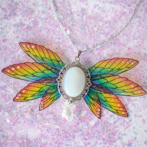 May include: A silver necklace with a white opal pendant set in a filigree frame. The pendant is surrounded by a rainbow-coloured, glittery, butterfly wing design.