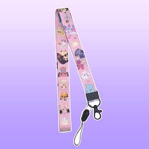 Puede incluir: Lanyard rosa con un patrón repetido de personajes de dibujos animados. El lanyard tiene un clip negro y un gancho giratorio desmontable.