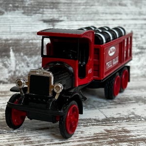 May include: A red and black vintage toy truck with the text "True Value" on the side. The truck has black tires and red wheels. The truck bed is filled with black tires. The truck has the number 13 on the side.