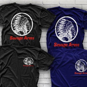 May include: Black and navy blue t-shirts with a white and red graphic. The graphic features a Native American profile inside a white circle, with the words "Savage Arms" in red below. The shirts are displayed on a white brick wall.