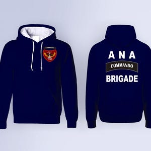 May include: Navy blue hooded sweatshirt with white drawstrings and a white interior. The front features a patch with a crest design. The back displays the text "ANA COMMANDO BRIGADE" in white lettering.