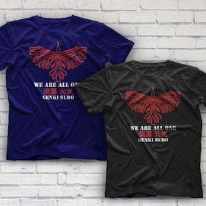 May include: Two t-shirts, one navy blue and one black, each featuring a red graphic of a stylized bird with outstretched wings. Below the graphic is the text "WE ARE ALL ONE" and Japanese characters, followed by "GENKI SUDO".