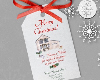 May include: A white gift tag with a red ribbon, featuring a watercolor illustration of a house with a Christmas wreath on the door. The text reads "Merry Christmas!" and "Warmest Wishes for the first Christmas in your new home!" with space for a name, broker/company, phone number, and optional 4th line.