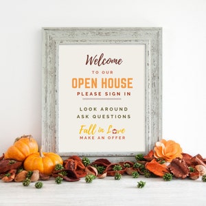 May include: A framed sign with the text "Welcome to our Open House Please Sign In Look Around Ask Questions Fall in Love Make an Offer" in a white frame with a white background. The sign is surrounded by fall-themed decorations, including pumpkins, cinnamon sticks, and dried leaves.