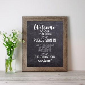 Op de afbeelding: Een rustiek houten bord met een zwarte lijst en een zwart bord met witte tekst die luidt: "Welkom bij onze open huis. Meld je aan. Neem een kijkje, stel vragen, neem een hapje, doe een bod. Dit zou je nieuwe huis kunnen zijn!"