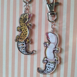 Könnte beinhalten: Zwei Leopardgecko-Schlüsselanhänger mit silbernen Karabinerhaken. Der Gecko links ist in traditionellem Braun und Orange mit schwarzen Flecken. Der Gecko rechts ist weiß mit schwarzen Flecken.