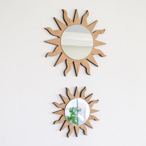 May include: Two wooden sun-shaped mirrors with a reflective surface. The larger mirror is on top and the smaller mirror is below it.
