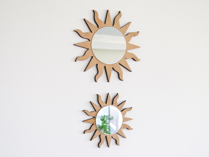 May include: Two wooden sun-shaped mirrors with a reflective surface. The larger mirror is on top and the smaller mirror is below it.