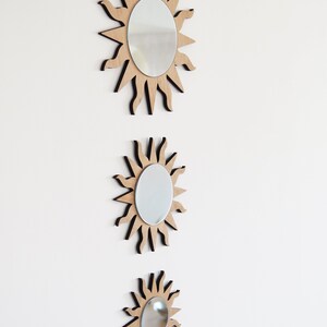 May include: Three wooden sunburst mirrors of varying sizes, each with a round mirror in the center. The mirrors are arranged vertically, with the largest at the top and the smallest at the bottom.