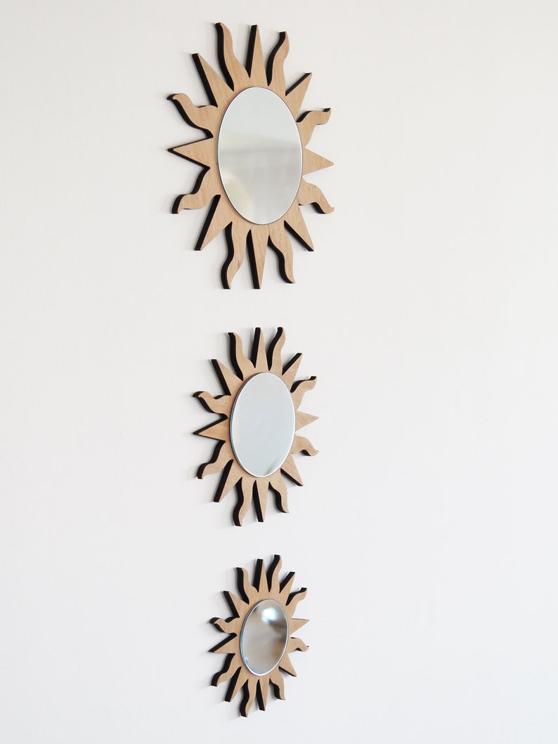May include: Three wooden sunburst mirrors of varying sizes, each with a round mirror in the center. The mirrors are arranged vertically, with the largest at the top and the smallest at the bottom.