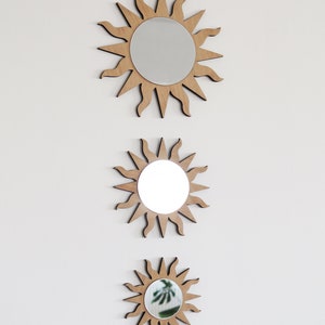 May include: Three wooden sun-shaped mirrors of varying sizes, each with a round mirror in the center. The mirrors are arranged vertically, with the largest at the top and the smallest at the bottom.