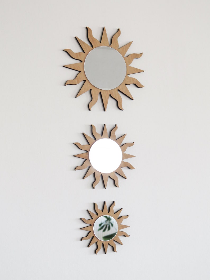 May include: Three wooden sun-shaped mirrors of varying sizes, each with a round mirror in the center. The mirrors are arranged vertically, with the largest at the top and the smallest at the bottom.