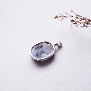 May include: A silver pendant with a white and black dendritic agate stone.