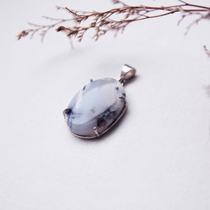 May include: A white and gray oval pendant with a silver setting. The pendant is hanging from a silver chain.