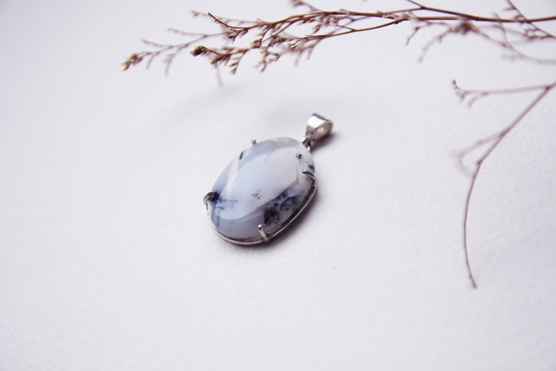 May include: A white and gray oval pendant with a silver setting. The pendant is hanging from a silver chain.