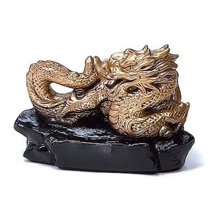 May include: A golden dragon figurine with intricate details, resting on a black, rock-like base. The dragon is posed in a coiled position, showcasing its scales and features. The sculpture is a decorative item.