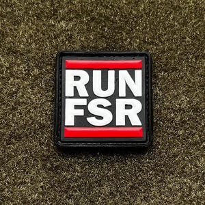 May include: A square patch with the text "RUN FSR" in white block letters. The text is set against a black background with a red stripe above and below the text. The patch is on a textured, olive-green surface.