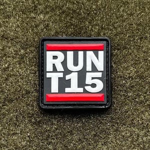 May include: A square patch with the text "RUN T15" in white block letters. The patch has a black border with red horizontal bars above and below the text. The background is a textured olive green.