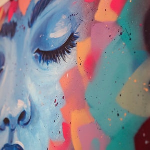 May include: Close-up of a colorful abstract painting featuring a woman's face with closed eyes. The painting is done in shades of blue, pink, yellow, and green, with splashes of white paint.