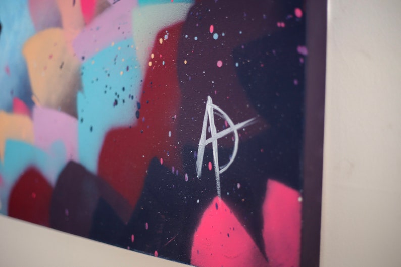 May include: Abstract painting with a colorful background of pink, blue, and red. The painting is signed with a white "A" in the lower right corner.