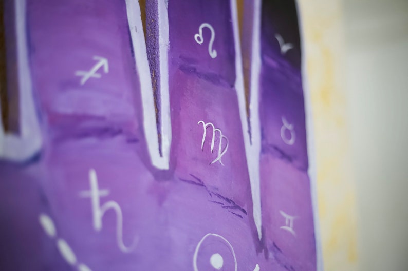 Puede incluir: Primer plano de una superficie pintada de p&uacute;rpura con s&iacute;mbolos del zod&iacute;aco blancos. El s&iacute;mbolo de Virgo es visible en el centro de la imagen.