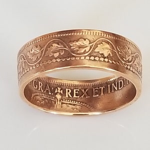 May include: A gold-colored ring with an engraved floral pattern around the band. The ring has the inscription "GRA: REX ET IND:" inside. The ring is displayed on a white surface.