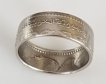 May include: A silver-colored ring with engraved Arabic text and decorative patterns. The ring has a wide band design and appears to be made from a coin. The ring is displayed on a white surface.