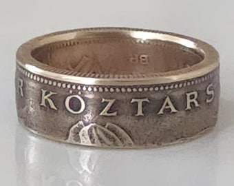 Könnte beinhalten: Ein silberner Ring mit goldener Innenseite. Der Ring hat einen geprägten Text und ein Bergdesign. Der Ring ist im Bandstil gehalten und scheint aus einer Münze gefertigt zu sein. Der Ring befindet sich auf weißem Hintergrund.