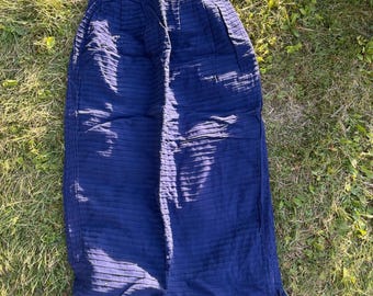 May include: A dark blue midi skirt featuring a high-waisted design with vertical pleats at the waistline and a textured, horizontal ribbed pattern throughout the fabric. The skirt has a straight silhouette and small side slits at the bottom hem.