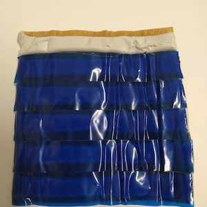 Op de afbeelding: Een close-up van een gelaagd materiaal in blauw en bruin met een witte laag in het midden. Het materiaal is gevouwen en heeft een textuur.