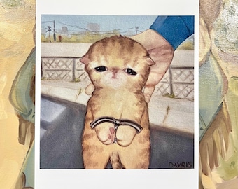 Peut inclure: Une peinture d'un petit chaton brun clair avec une expression triste, portant des menottes. Le chaton est tenu par une main portant une chemise bleue. L'arrière-plan est une image floue d'une rue de la ville.