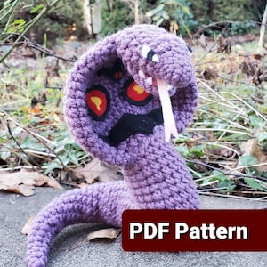 May include: Purple crocheted cobra snake amigurumi plush toy with red eyes and a black mouth. The snake is posed with its head raised and its tongue sticking out. The text "PDF Pattern" is visible in the bottom right corner of the image.