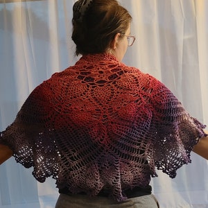 May include: A crocheted shawl with a gradient of red, pink, purple, and gray colors. The shawl has a lacy design and a scalloped edge.