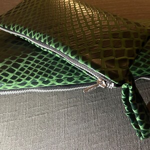 Pu&ograve; includere: Una pochette verde e nera con motivo a pelle di serpente e chiusura con cerniera.