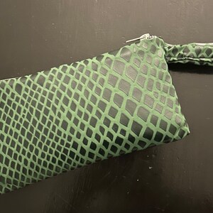 Pu&ograve; includere: Una pochette verde con motivo a pelle di serpente, chiusura con cerniera e manico superiore.