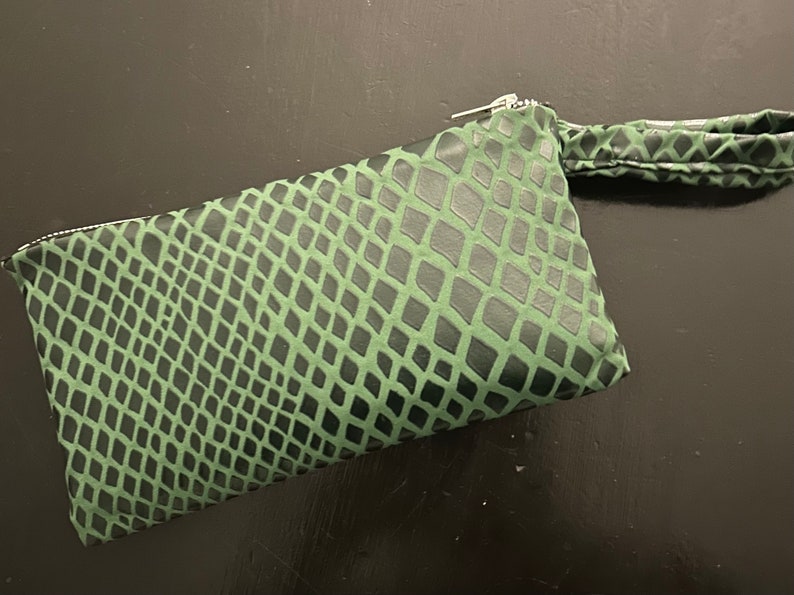 Pu&ograve; includere: Una pochette verde con motivo a pelle di serpente, chiusura con cerniera e manico superiore.