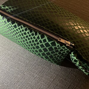 Pu&ograve; includere: Una pochette verde con cerniera a forma di pelle di serpente e una cerniera argentata.