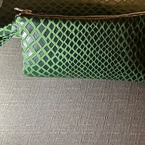 Pu&ograve; includere: Una pochette verde con cerniera a forma di pelle di serpente con un piccolo manico.