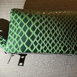 Pu&ograve; includere: Una pochette verde con motivo a pelle di serpente, chiusura con cerniera e un cinturino da polso abbinato.