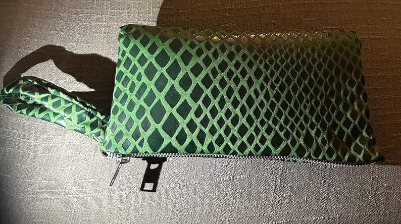 Pu&ograve; includere: Una pochette verde con motivo a pelle di serpente, chiusura con cerniera e un cinturino da polso abbinato.
