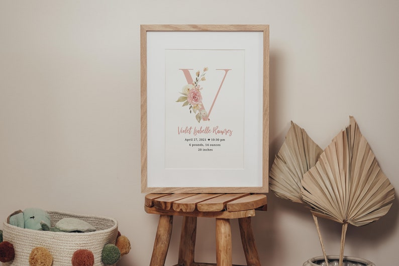 Pink floral monogram birth details print. Name written in cursive font. Print is in a natural wooden frame.