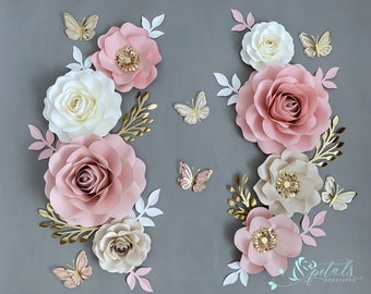 May include: A set of paper flowers in shades of pink, white, and gold. The flowers are arranged in a cluster, with butterflies scattered around them. The flowers are made of paper and have a delicate, layered look. The butterflies are also made of paper and have a whimsical, fairy-like quality.