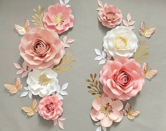 May include: A set of paper flowers in shades of pink and white, with gold accents. The flowers are arranged in a decorative pattern on a gray background.