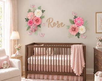 May include: A dark wood crib with a pink ruffled skirt and a textured pink blanket. Above the crib, two large floral arrangements made of paper flowers in shades of pink, cream, and green, with small butterflies and the wooden name Rose.