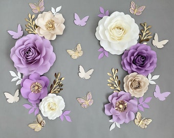 May include: A set of paper flowers in shades of purple, cream, and gold with butterflies. The flowers are arranged in a symmetrical pattern on a gray background.