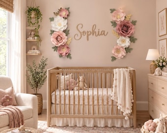 Puede incluir: Una cuna de madera con falda blanca con volantes y una manta de punto color crema. Sobre la cuna, el nombre Sophia está escrito en letras de madera en cursiva, flanqueado por dos grandes arreglos de flores de papel.