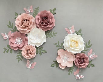 May include: A set of paper flowers in shades of pink and white with butterflies. The flowers are arranged in a cluster and are made of paper. The butterflies are also made of paper and are in various sizes.